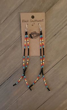 a pair of beaded earrings on top of a wooden table next to a card