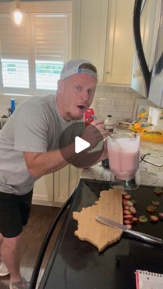 a man standing in front of a kitchen counter holding an apple and milkshake