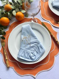 an orange and white table setting with napkins, silverware, and citrus fruit