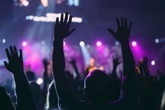 people raising their hands at a concert with bright lights in the backgrounnd