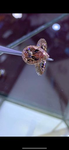 a pink diamond ring sitting on top of a glass display case in a jewelery shop