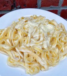 a white plate topped with pasta covered in sauce on top of a red brick wall