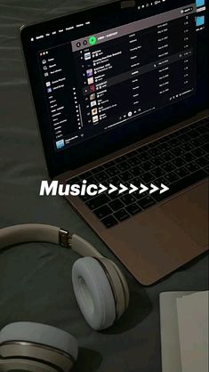 an open laptop computer sitting on top of a table next to headphones and a book