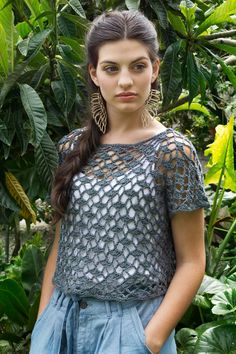 a woman standing in front of green plants and trees with her hands on her hips