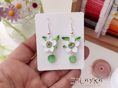 a pair of green and white flower earrings on a card with sprinkles