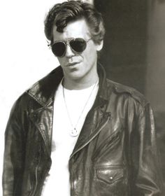 black and white photograph of a man in sunglasses wearing a leather jacket, t - shirt and jeans