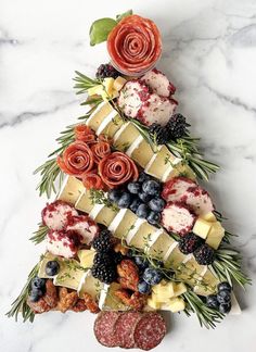 a christmas tree made out of cheeses, berries and meats on a marble table