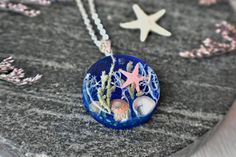 Bring a piece of the ocean with you wherever you go with our Pressed Flower "Under the Ocean" Pendant. This unique and eye-catching pendant features real blue lichen, starfish, sand, sea shells and abalone shells encased in eco-friendly resin colored with transparent inks to give it a sparkling water effect.The pendant comes with a  -1.5mm chain, 18" long, but if you prefer a different length, you can type it in the personalization box.  The pendant is available with  -925 sterling silver or  -s Turquoise Starfish Ocean-inspired Jewelry, Ocean-inspired Turquoise Necklace With Starfish Charm, Turquoise Ocean-inspired Necklace With Starfish Charm, Turquoise Necklace With Starfish Charm, Ocean-inspired Jewelry For Vacation, Handmade Ocean Colored Pendant Jewelry, Handmade Ocean Color Pendant Jewelry, Handmade Ocean Color Strand Jewelry, Handmade Strand Ocean Color Jewelry