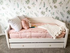 a white daybed with pink sheets and pillows on it in front of a floral wallpaper