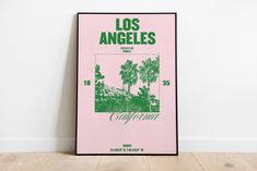 a pink poster with the words los angeles written in green on it, against a white wall