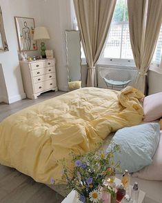 there is a bed with yellow sheets and pillows on the floor next to a window