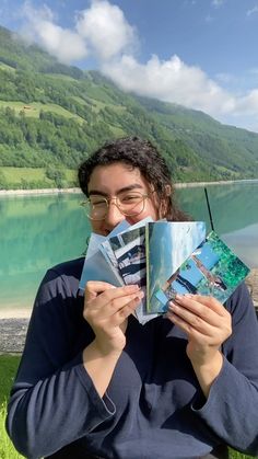 a woman sitting on the grass holding up two photos in front of her face and looking at them