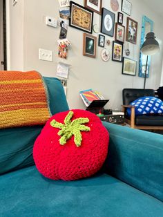 a red knitted strawberry pillow sitting on top of a blue couch in a living room