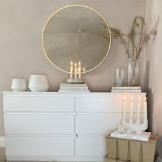 a white dresser topped with candles and a round mirror