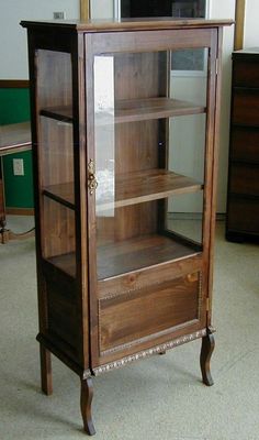 an old wooden cabinet with glass doors and drawers in a room that has carpeted flooring