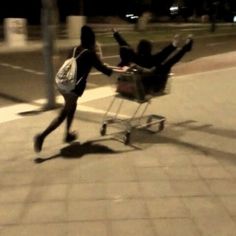 two people pushing a shopping cart down the street with their legs in the air and one person laying on it's back