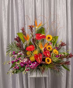 a vase filled with lots of colorful flowers on top of a white table next to a curtain