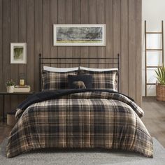 a bed with plaid comforter and pillows in a room next to a wooden wall