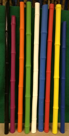 several different colored plastic pens lined up against a green wall with blue, yellow, red, and orange sticks sticking out of them