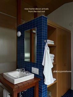 a bathroom with blue tile and wooden shelves, white towels hanging on the rack next to the sink