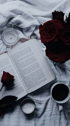 an open book and two candles on a bed with roses, teacups and saucers