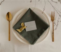 a white plate topped with a napkin and gold utensils next to a green napkin