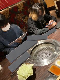 two people sitting at a table with food in front of them on their cell phones