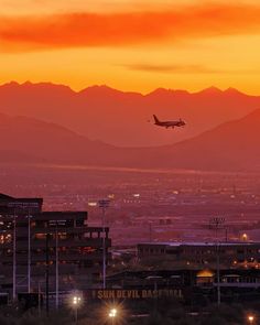 an airplane is flying in the sky at sunset with mountains in the background and lights on