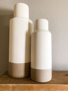 two white vases sitting on top of a wooden shelf