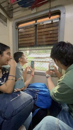 three people sitting on a train looking at their cell phones and taking pictures with them