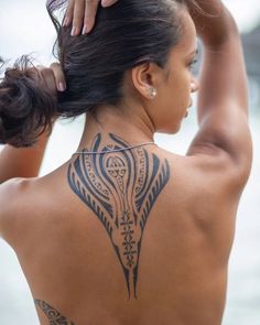 a woman with a tattoo on her back is holding her hair in one hand and looking at the other