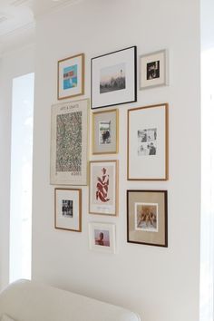 a white couch sitting under a wall covered in pictures and framed art on it's side