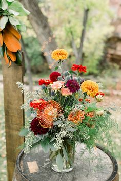 a vase filled with lots of flowers sitting on top of a wooden table next to a tree