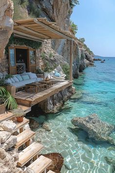 a house sitting on top of a rocky cliff next to the ocean with clear blue water