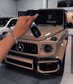 a hand holding a cell phone in front of a mercedes car