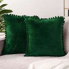 two green pillows sitting on top of a white couch next to a potted plant