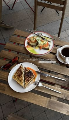 two plates with food on them sitting on a wooden table next to a cup of coffee