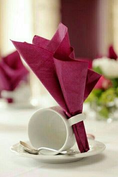 an origami flower is placed in a white plate on a table with pink napkins