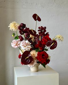 a vase filled with lots of different colored flowers on top of a white table next to a wall