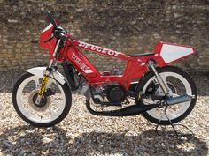 a red motorcycle parked on top of a gravel covered ground next to a stone wall