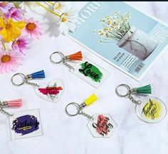 four keychains with different designs on them sitting next to flowers and a book