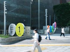 people walking on the sidewalk in front of an office building with colorful signs and letters