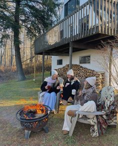 three people sitting around a fire pit in front of a house with a deck on top