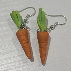 two carrot shaped earrings with green stems hanging from hooks