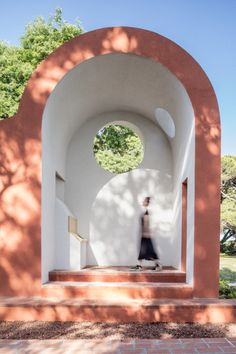 a woman walking through an archway in the middle of a park