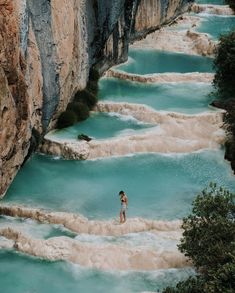 a woman standing on the edge of a cliff next to blue water and rocky cliffs