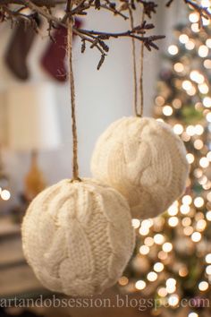 two knitted balls hanging from a tree with christmas lights in the backgroud