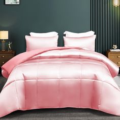 a bed with pink comforter and pillows in a room next to a lamp on a table