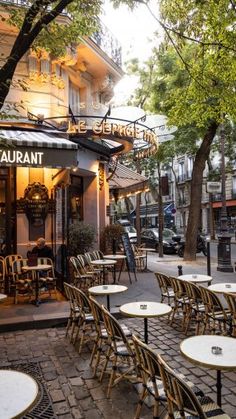 an outdoor restaurant with tables and chairs on the sidewalk in front of it, surrounded by trees