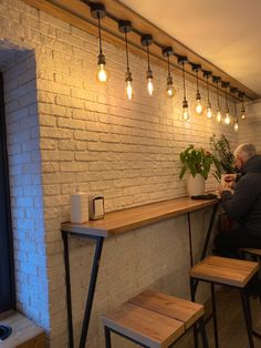 a man sitting at a table in front of a white brick wall with lights hanging from it